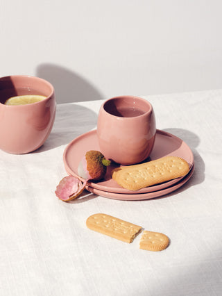 A rose small ceramic cup, peeled lychee, and biscuit on 2 small stacked plates on a white table cloth.