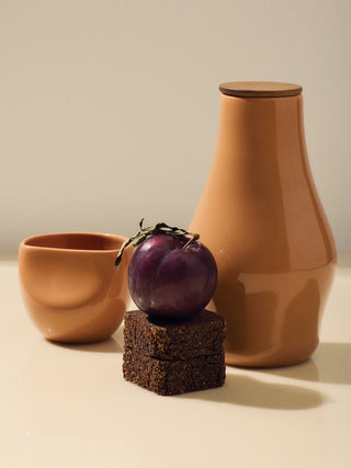 One Amaretto Carafe next to one Amaretto Medium Cup. A piece of brownie and a plum are featured in the center.