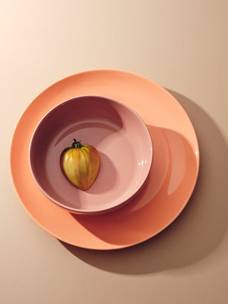 Rose colored bowl on a coral colored plate with half a yellow tomato inside