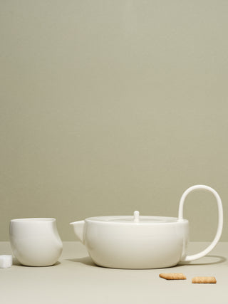A medium white cup next to a large white teapot