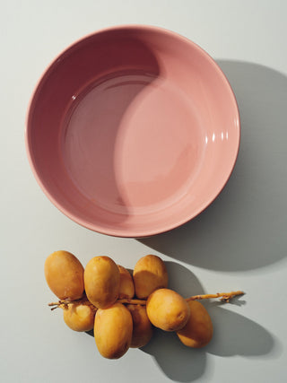 Rose colored bowl next to branch of pears