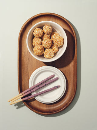 An open lidded bowl filled with small seed balls on top of oval wooden tray