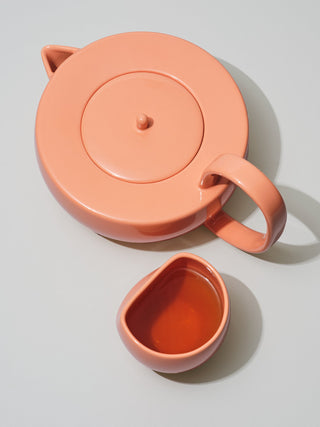 Large coral teapot next to asymmetrical cup