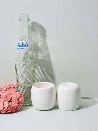 Short white ceramic cups next to empty vintage soda bottle and pink pumpkin seeds