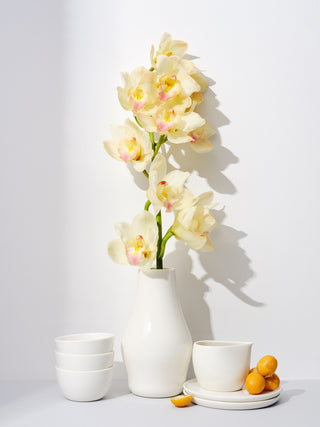 An arrangement of white dishes, with a white carafe in the center with a branch of flowers