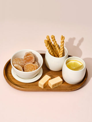 Two white small cups and a switch bowl with snacks on a small wooden tray