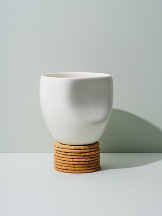 White ceramic cup with recessed side on stack on crackers