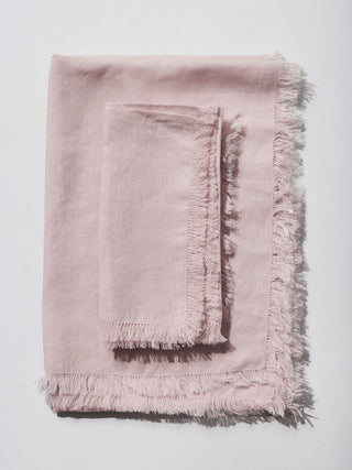 Blush linen napkin folded on top of blush linen runner.