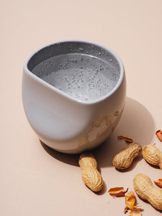 One grey medium cup filled with sparkling water next to peanuts