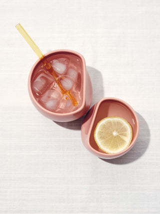Top view of two mauve asymetical ceramic cups full of water, one with ice and a straw and one with lemon.
