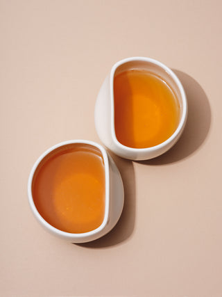 Two white asymmetrical cups holding orange tinted tea