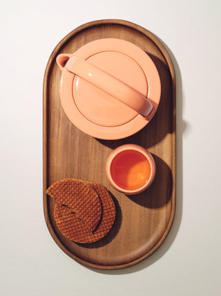 A small teapot, cup, and waffle treat on top of oval wooden tray