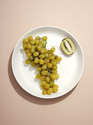 Shallow serving bowl with bunch of green grapes an half a kiwi