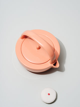 Coral ceramic teapot and a white frosted cupcake