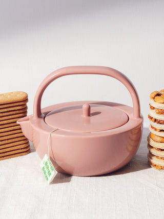Rose ceramic teapot with teabag poking out surrounded by stacked biscuits