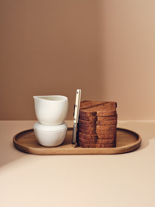 Stack of white ceramic and bread on oval wooden tray